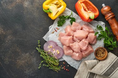 Tahtadaki tavuğun çiğ parçaları, baharatlar, otlar ve sebzeler koyu gri arka planda. Gulaş ya da şiş kebap için ham malzeme. Üst Manzara. Boş kopyalama alanı.