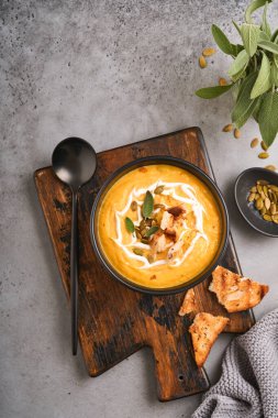 Balkabağı geleneksel çorbası kremalı ipeksi desenli adaçayı ve siyah tabakta kırmızı biber. Eski gri arka plan. Uzayı kopyala Model yap. Üst manzara, düz uzanma.