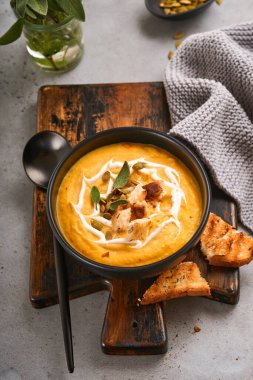 Balkabağı geleneksel çorbası kremalı ipeksi desenli adaçayı ve siyah tabakta kırmızı biber. Eski gri arka plan. Uzayı kopyala Model yap. Üst manzara, düz uzanma.