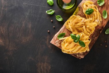 Tagliatelle. Ev yapımı makarna, fesleğen yaprağı, un, biber, zeytinyağı, vişneli domates ve siyah ahşap arka planda merdane ve makarna bıçağı. Yemek konsepti. Model yap. Kopyalama alanı ile yatay.