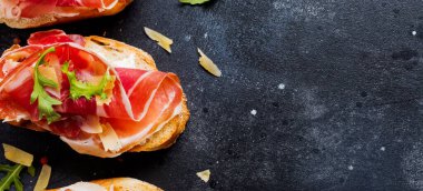 Jamon, roka ve beton eski koyu arka plan üzerinde sert peynir ile açık sandviçler. Rustik tarzı. Üstten Görünüm.