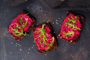 Bruschetta karanlık beton zemin üzerine kırmızı pancar Humus, roka ve susam tohumu ile. Üstten görünüm.