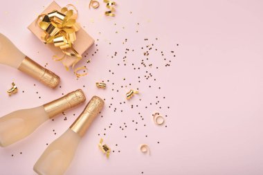 Şampanya şişesi, hediye ya da hediye kutusu ve pembe arka planda altın parıldayan yıldız konfetisi. Noel ya da yeni yıl kompozisyonu ya da kartı. Kutlama düzlüğü. Parti yaratıcı konsepti. Üst görünüm.