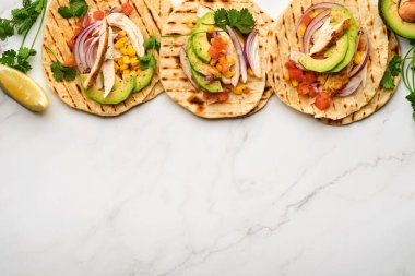 Beyaz taş masada ızgara tavuk, avokado, mısır taneleri, domates, soğan, kişniş ve salsa soslu Meksika tacoları. Geleneksel Meksika ve Latin Amerika sokak yemekleri. Üst görünüm.