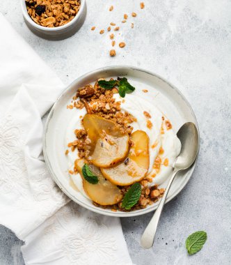 Gri seramik tabakta sağlıklı bir kahvaltı için karamelize armut, granola, fındık ve eritilmiş şeker içeren Yunan yoğurdu. Kırsal tarzda. Üst görünüm