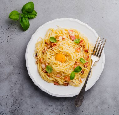 Makarna spagetti carbonara pastırma, kaşar peyniri, yumurta sarısı ve fesleğen ile ışık gri arka plan üzerinde bırakır. Geleneksel İtalyan yemeği. Üstten görünüm.