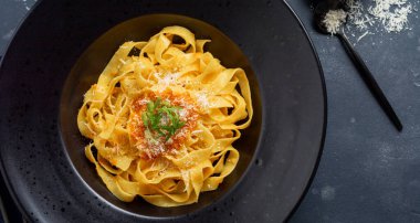 Fettuccine makarna ile geleneksel İtalyan Passat sos ve parmesan peynir koyu arka plan üzerinde siyah plaka. Üstten görünüm.