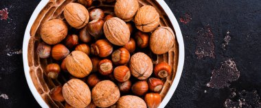 Sağlıklı çiğ fındık ve cevizleri kahverengi beton arka planda seramik tabakta karıştır. Üst görünüm.