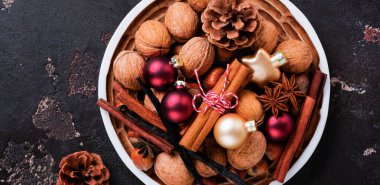 Sağlıklı ham fındık ve ceviz, tarçın karışımı sopa, anason, vanilya, çikolata ve seramik plaka kahverengi beton zemin üzerinde Noel oyuncaklar. Üstten görünüm.