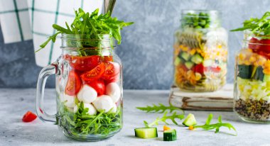 İtalyan roka salatası, mozzarella ve masada öğle yemeği için kavanozda servis edilen vişneli domates. Seçici odak.