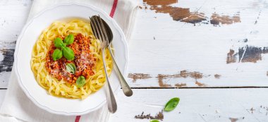 Hafif ahşap arka plan üzerinde beyaz bir tabakta bolonya sos, fesleğen ve parmesan peyniri ile geleneksel İtalyan çanak fettuccine makarna. Üstte görüntü.