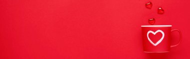 Kırmızıda ya da kırmızı arka planda boyalı kalbi, şekeri ve çikolatası olan kırmızı bardak. Düz kompozisyon. Sevgililer Günü konsepti. Üst görünüm, alanı kopyala.