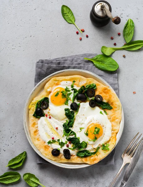 Türk yumurtaları yoğurt, peynir, zeytin, ıspanak ve gri arka planda seramik vintage tabakta kırmızı biber. Üst görünüm.