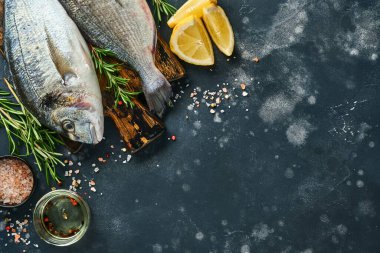 Çiğ dorado taze balığı ya da limon, kekik, sarımsak, kiraz, domates ve tuz yapımında kullanılan malzemelerle birlikte siyah kayalık, taş ya da beton zemin. Kopyalama alanı olan üst görünüm.