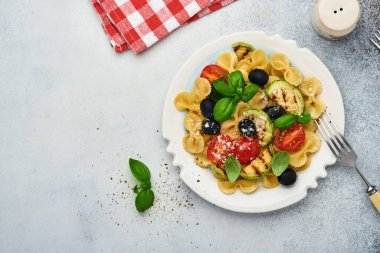 Sebzeli makarna fiocchi salatası ızgara kabak, vişneli domates, zeytin, fesleğen ve parmesan peyniri beyaz tabakta taş ya da beton arka planda. Yemek konsepti. Üst görünüm