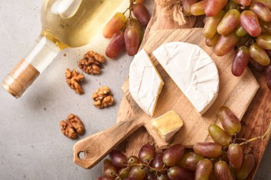 Üzümlü iki şarap şişesi, peynirli camembert peyniri, fındık ve şarap bardakları eski gri beton masa zemininde fotokopi alanı ile. Asma dallı kırmızı şarap. Şarap kompozisyonu. Model.
