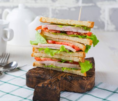 Kahvaltıda içi jambonlu domatesli sandviç ve hafif ahşap arka planda marul. Seçici odak.