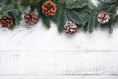 Noel süslemesi. Altın takılar, koniler, çanlar, köknar dalları ve eski beyaz tahta arka planda sunulan bayram süsleri. Sınır tasarımı. Üst Manzara. Model.