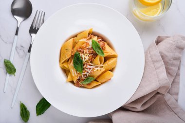Bolonez Penne Pastası. Parmesan peynirli, fesleğenli ve bolonez soslu leziz iştah açıcı İtalyan makarna. Taş masa üzerinde beyaz tabak geleneksel İtalyan mutfağı. Üst görünüm