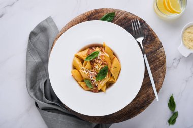 Bolonez Penne Pastası. Parmesan peynirli, fesleğenli ve bolonez soslu leziz iştah açıcı İtalyan makarna. Taş masa üzerinde beyaz tabak geleneksel İtalyan mutfağı. Üst görünüm