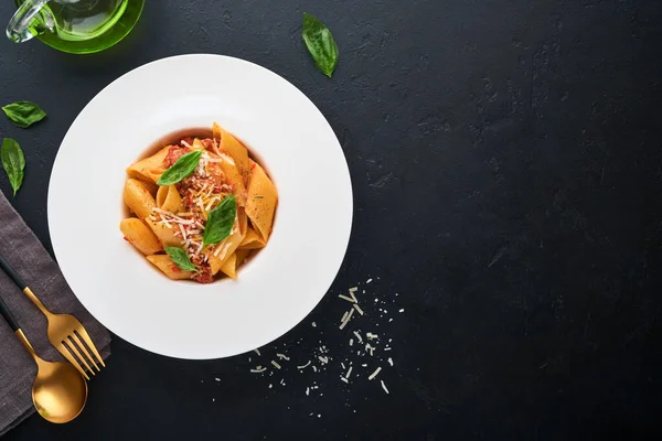 stock image Bolognese Penne Pasta. Tasty appetizing classic italian penne pasta with parmesan, basil and Bolognese sauce in white plate on plate on black dark background.Traditional Italian cuisine. Top view.