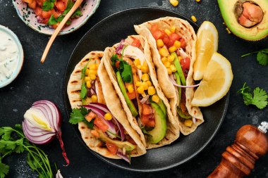 Meksika tacoları, ızgara tavuk, avokado, mısır taneleri, domates, soğan, kişniş ve siyah taş masada salsa. Geleneksel Meksika ve Latin Amerika sokak yemekleri. Üst görünüm.