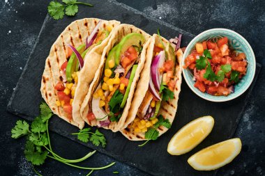 Meksika tacoları, ızgara tavuk, avokado, mısır taneleri, domates, soğan, kişniş ve siyah taş masada salsa. Geleneksel Meksika ve Latin Amerika sokak yemekleri. Üst görünüm.