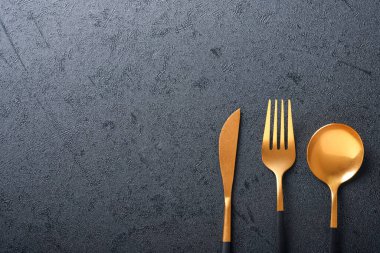 Altın kaşık, çatal ve bıçak. Siyah arka planda siyah ve altın çatal bıçak seti. Modaya uygun ve lüks bir yemek. Üst Manzara. Metnin için boşluk kopyala.