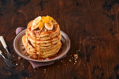 Krepler. Koyu ahşap zemin üzerinde kahvaltıda muz, ceviz ve karamel ile ev yapımı pofuduk krep. Geleneksel Amerikan kahvaltısı için leziz krepler. Seçici odaklanma. Model.