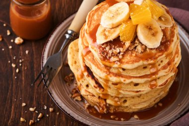 Krepler. Koyu ahşap zemin üzerinde kahvaltıda muz, ceviz ve karamel ile ev yapımı pofuduk krep. Geleneksel Amerikan kahvaltısı için leziz krepler. Seçici odaklanma. Model.