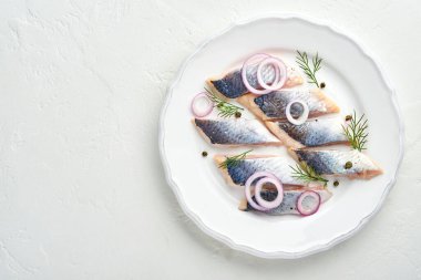 Ringa. Baharatlı tuzlu ringa balığı, otlar ve soğan beyaz tabakta, ışık taşından arka planda fotokopi alanı ile birlikte. Salamura edilmiş balık. Sağlıklı doymamış yağlı yiyecekler.