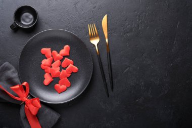 Siyah kaşık, çatal, bıçak, temiz siyah tabak ve kırmızı kalp süslemeli peçete. Sevgililer Günü seti siyah arka planda şık siyah ve altın çatal bıçak seti. Moda ve lüks yemek Üst Manzara