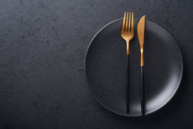 Altın kaşık, çatal, bıçak ve temiz boş siyah tabak. Siyah arka planda siyah ve altın çatal bıçak seti. Modaya uygun ve lüks bir yemek. Üst Manzara. Metnin için boşluk kopyala.