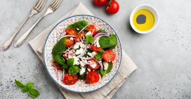 Domates, ıspanak yaprakları, kırmızı soğan ve beyaz peynirli salata gri artalanları üzerinde ışık seramik plaka üzerinde. Seçici odak. Üstten görünüm.