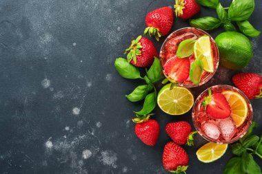 İki bardak punç ve limonata, arınma suyu ya da kokteyl yapmak için taze malzeme. Çilek, kireç, nane, fesleğen, buz küpü ve siyah taş ya da beton zemin üzerinde titretici. Üst görünüm.