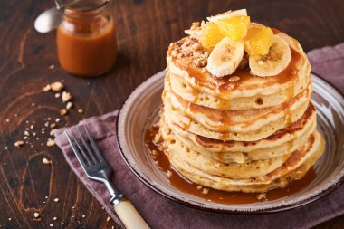 Krepler. Koyu ahşap zemin üzerinde kahvaltıda muz, ceviz ve karamel ile ev yapımı pofuduk krep. Geleneksel Amerikan kahvaltısı için leziz krepler. Seçici odaklanma. Model.