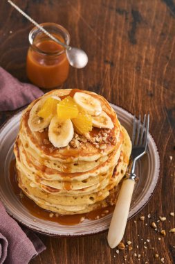 Krepler. Koyu ahşap zemin üzerinde kahvaltıda muz, ceviz ve karamel ile ev yapımı pofuduk krep. Geleneksel Amerikan kahvaltısı için leziz krepler. Seçici odaklanma. Model.