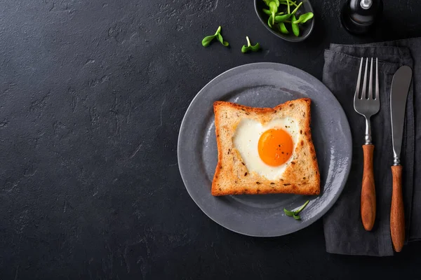 Sevgililer Günü 'nde kahvaltı. Kalp şeklinde sahanda yumurta ve ekmek ve siyah arka planda taze sebze. Sevdikleri için sürpriz kahvaltı. Üst Manzara. Model.