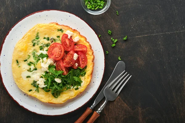 Köy usulü omlet ya da yeşil soğanlı frittata peynirli mozzarella, yeşil roka ve eski ahşap arka planda domatesler. Sağlıklı gıda konsepti. Kahvaltıda. Uzayı kopyala Üst Manzara. Model.