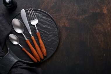 Klasik çatal bıçak takımı. Siyah ahşap arka planda ahşap tabakta ahşap kaşık ve çatal. Boş tabaklar. Üst Manzara. Model.