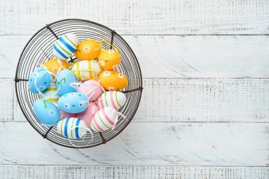 Paskalya tatili. Beyaz ahşap arka planda demir sepette renkli Paskalya yumurtaları. Paskalya tebrik kartı. Üst görünüm, alanı kopyala.
