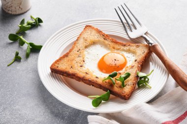 Sevgililer Günü 'nde kahvaltı. Kalp şeklinde yumurtalı tost ve açık gri arka planda mikro yeşillikler, kahvaltı masası üstü. Sevgililer Günü kahvaltısı. Üst Manzara. Model.