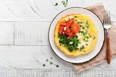 Yeşil soğanlı omlet veya frittata, peynir mozzarella, yeşil roka ve eski ahşap arka planda domates. Sağlıklı gıda konsepti. Kahvaltıda. Uzayı kopyala Üst Manzara. Model.
