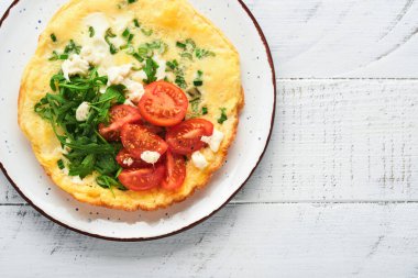 Yeşil soğanlı omlet veya frittata, peynir mozzarella, yeşil roka ve eski ahşap arka planda domates. Sağlıklı gıda konsepti. Kahvaltıda. Uzayı kopyala Üst Manzara. Model.
