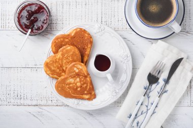 Böğürtlen reçelli krep ve kalp şeklinde bal ve beyaz ahşap zemin üzerinde sıcak bir fincan kahve. Sevgililer Günü için konsept kahvaltı ya da yukarıdan bakıldığında sevilen bir masa için hoş bir sürpriz
