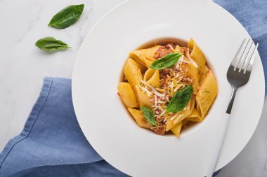 Bolonez Penne Pastası. Lezzetli iştah açıcı klasik İtalyan makarna parmesan peyniri, fesleğen ve Bolonez sosu ile taş masada beyaz tabakta. Geleneksel İtalyan mutfağı Üst Manzara