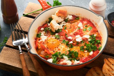 Shakshuka ev yapımı sahanda yumurta, domates sosu, zeytinyağı, biber, soğan ve sarımsak eski gri arka planda demir kızartma tavasında. Geleneksel İsrail mutfağı. Geç kahvaltı konsepti