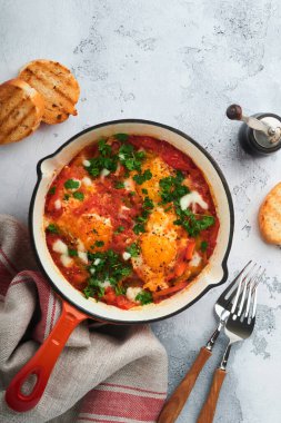 Shakshuka. Hafif gri kayrak, taş ya da beton zemin üzerinde demir tavada sebzeli sahanda yumurta. Geleneksel İsrail mutfağı. Geç kahvaltı konsepti. Üst görünüm, afiş