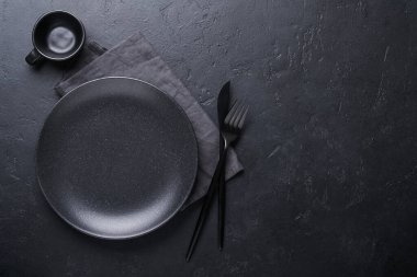 Siyah kaşık, çatal, bıçak ve temiz boş siyah tabak. Siyah arka planda siyah ve altın çatal bıçak seti. Modaya uygun ve lüks bir yemek. Üst Manzara. Metnin için boşluk kopyala.