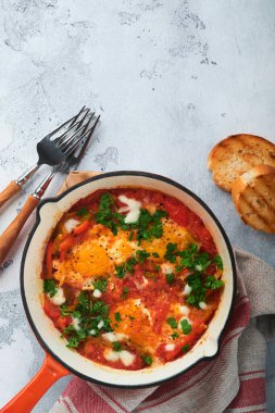 Shakshuka. Hafif gri kayrak, taş ya da beton zemin üzerinde demir tavada sebzeli sahanda yumurta. Geleneksel İsrail mutfağı. Geç kahvaltı konsepti. Üst görünüm, afiş